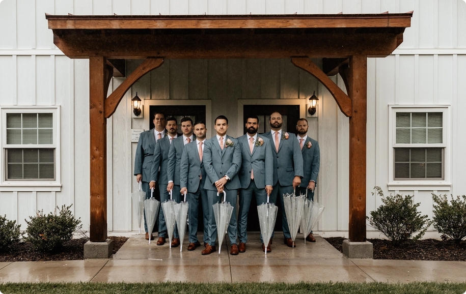 Groomsmen wedding group pose in light blue suits with blush ties and brown shoes posing with umbrellas.