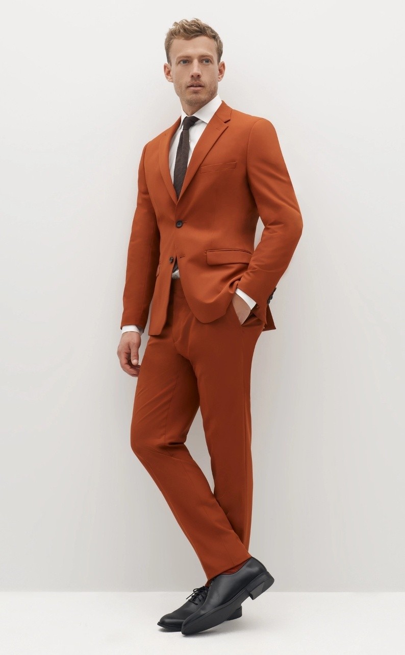 Man wearing special order color rust terracotta suit with notch lapel, black tie, and black dress shoes.